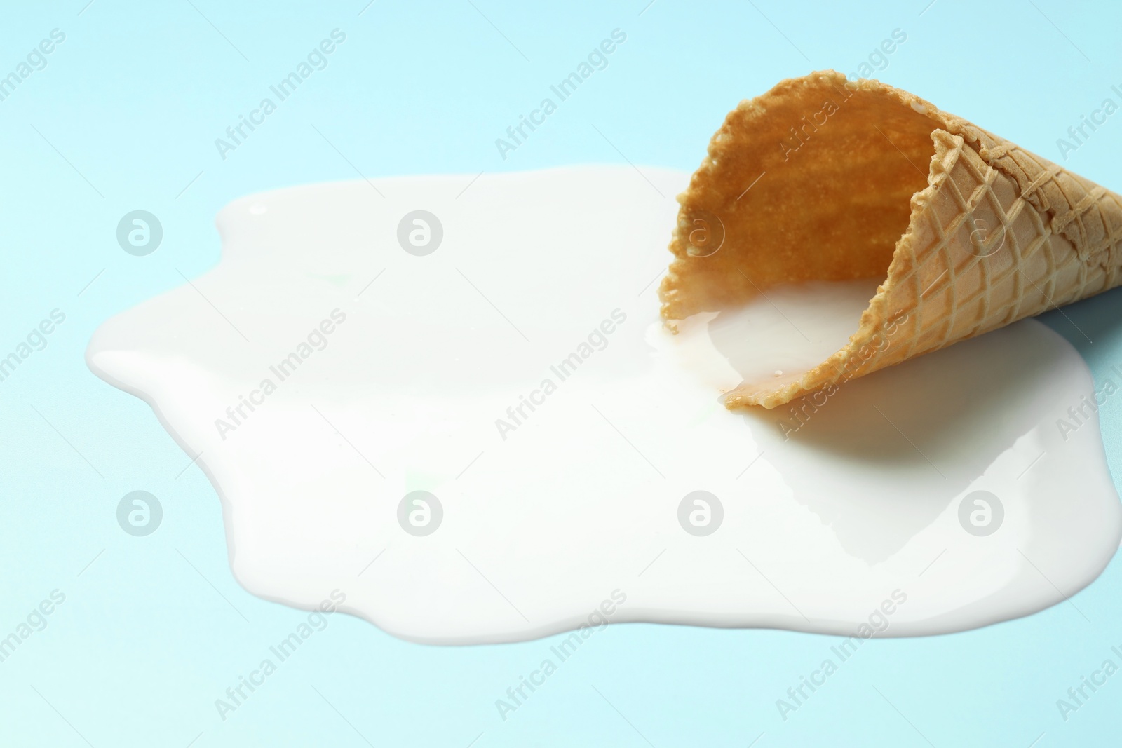 Photo of Melted ice cream and wafer cone on light background, closeup