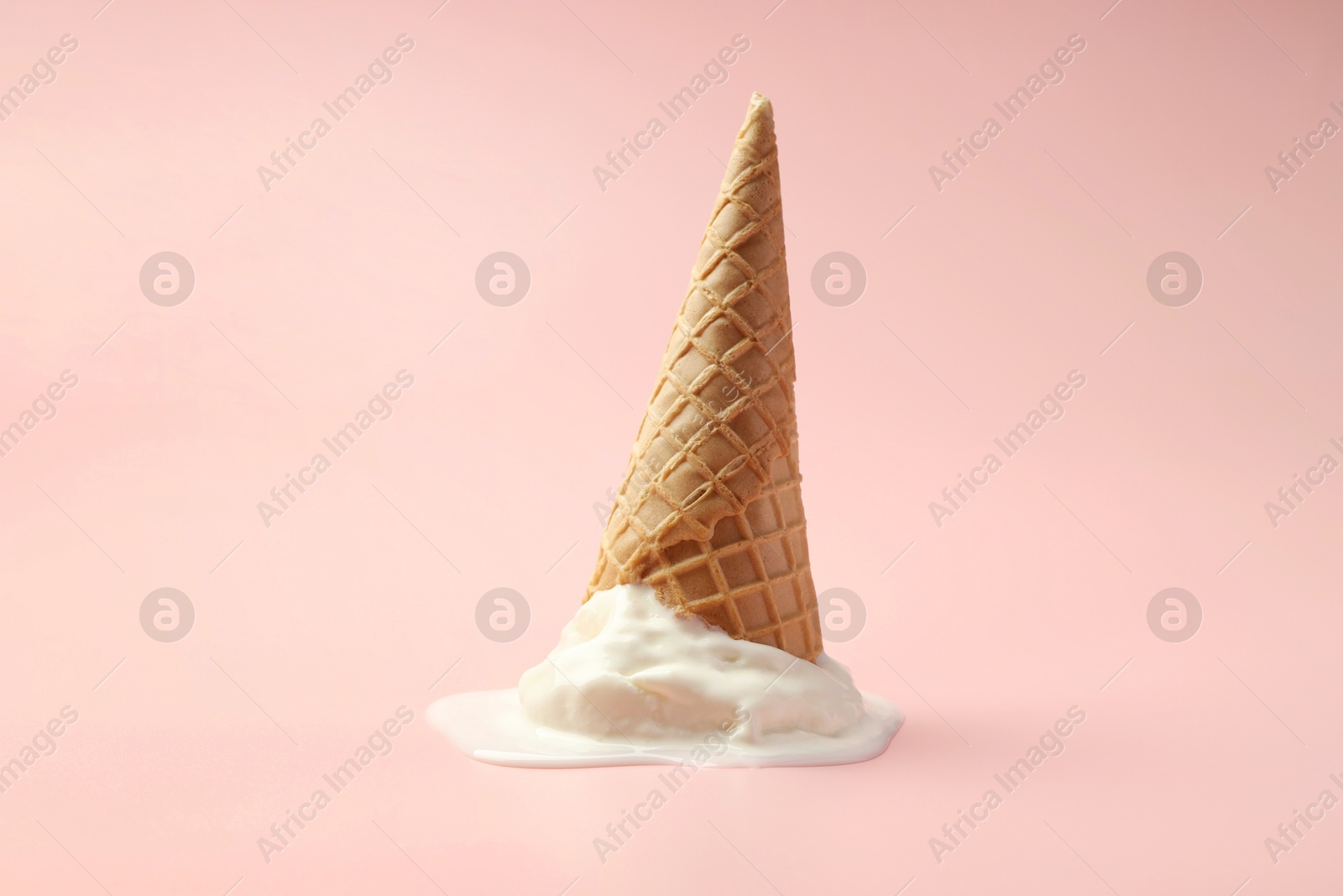 Photo of Melted ice cream in wafer cone on light pink background