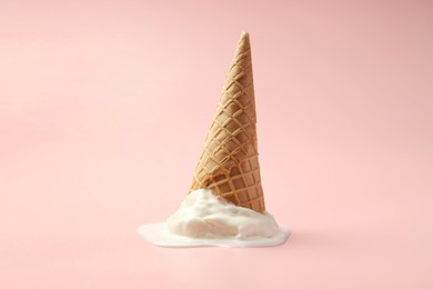 Melted ice cream in wafer cone on light pink background