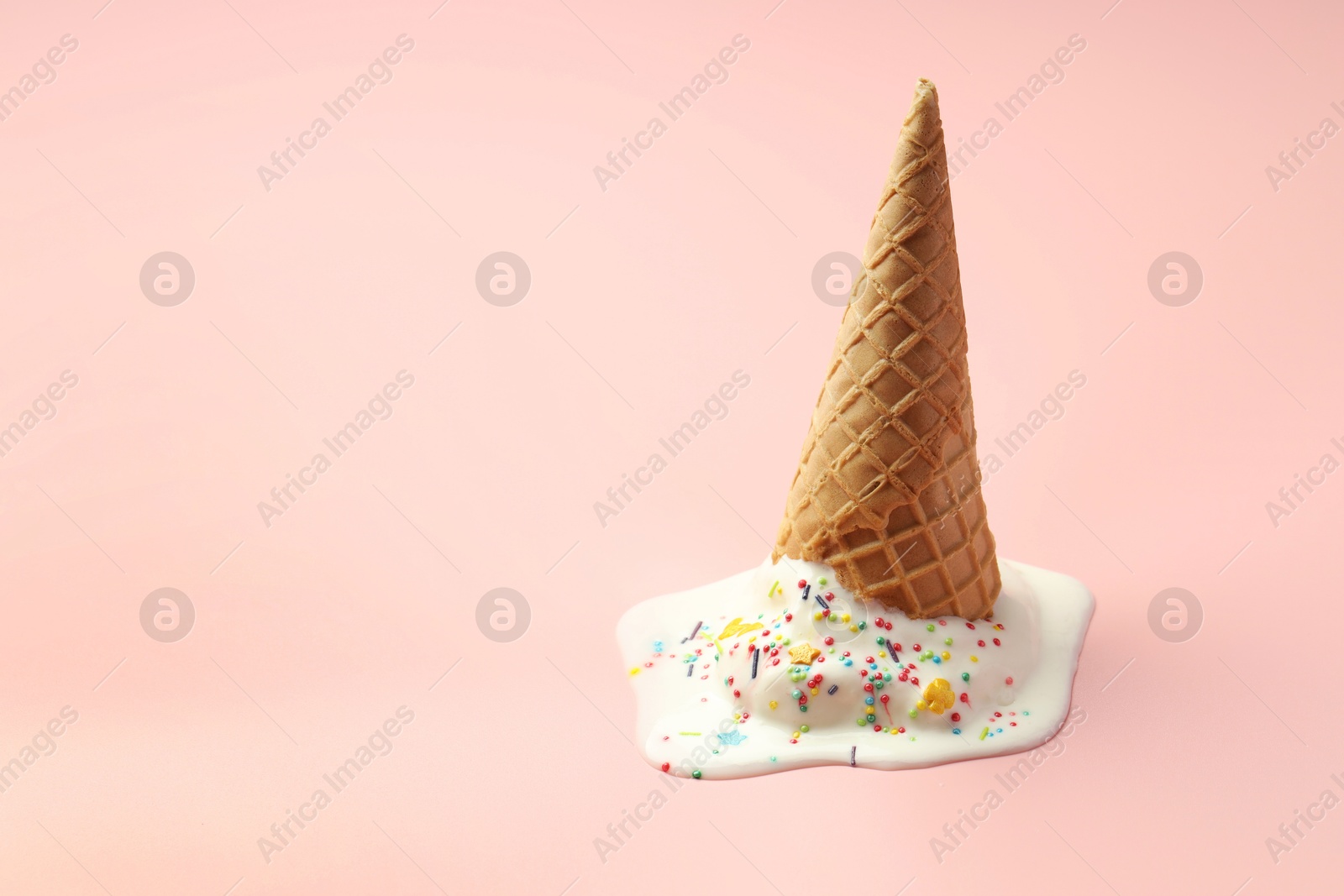 Photo of Melted ice cream in wafer cone on light pink background. Space for text