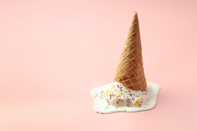 Melted ice cream in wafer cone on light pink background. Space for text