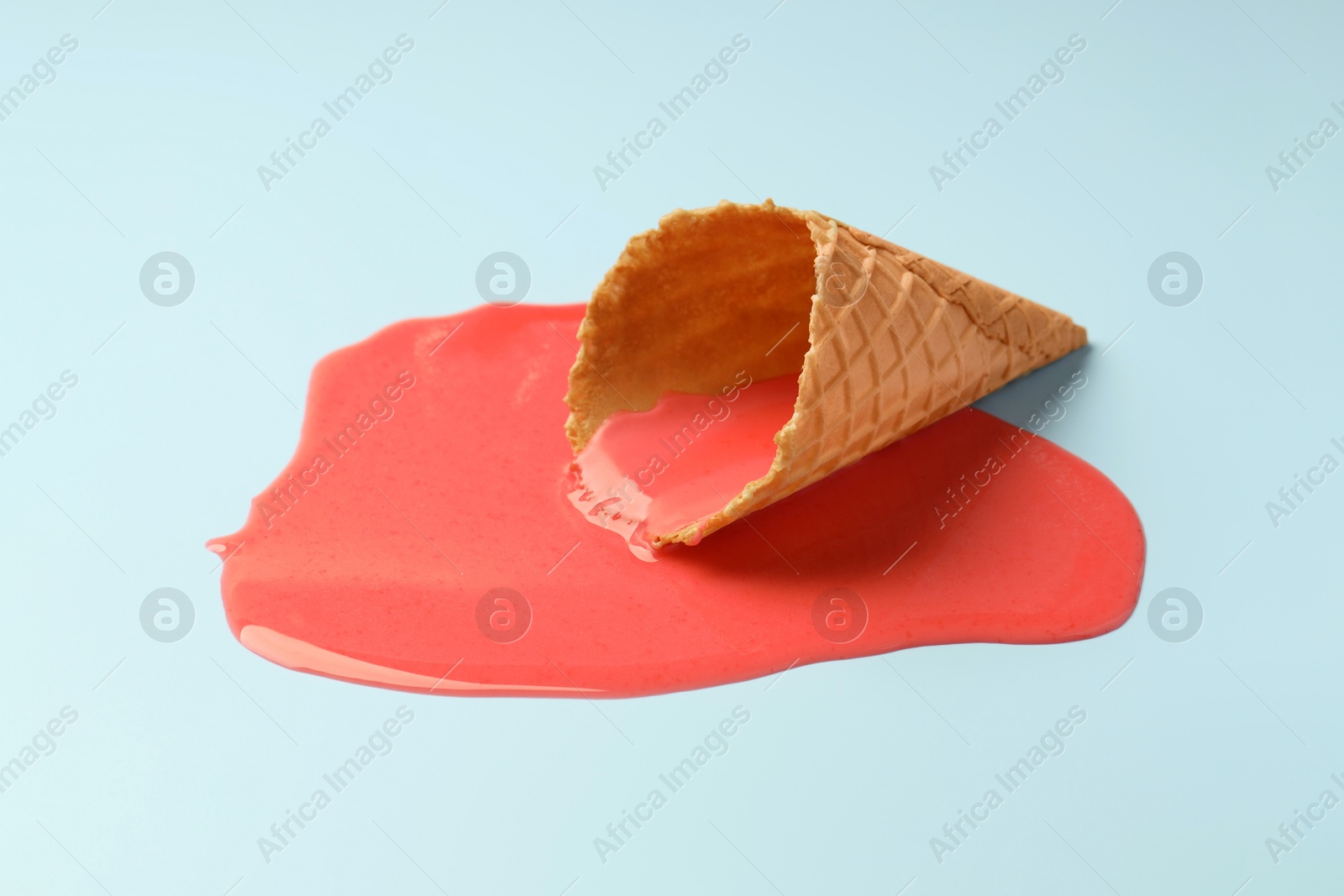 Photo of Melted ice cream and wafer cone on light blue background