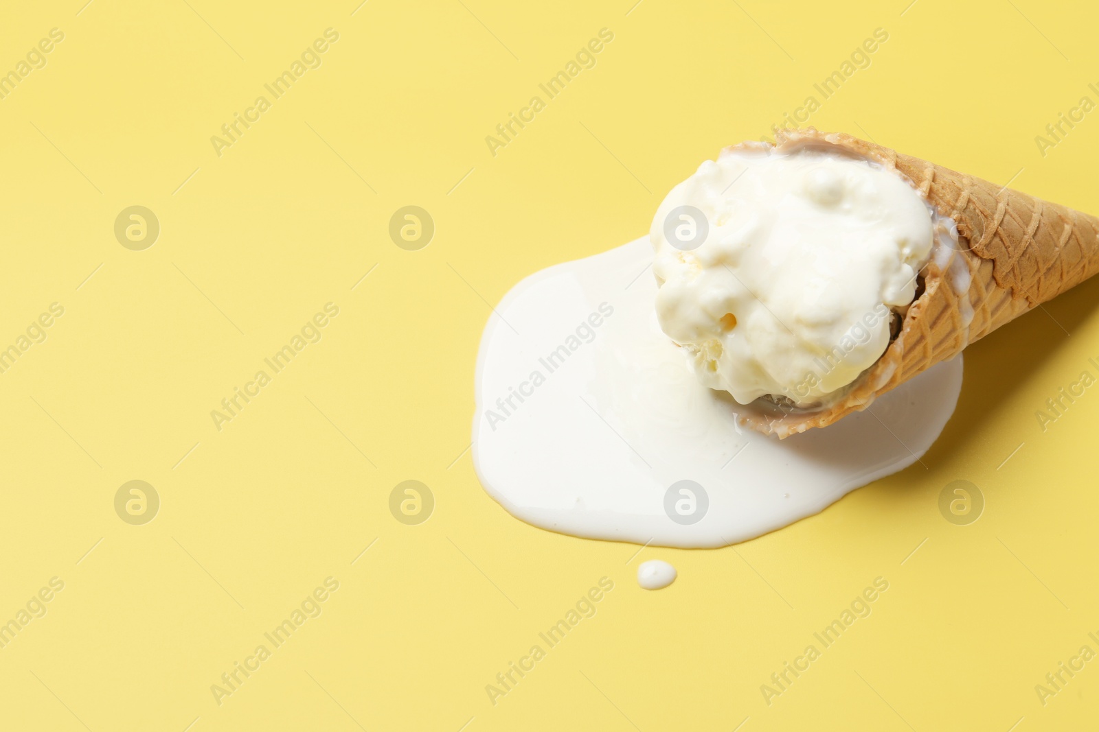 Photo of Melted ice cream in wafer cone on yellow background. Space for text