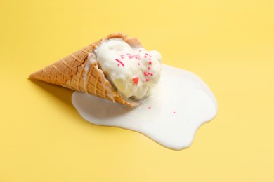 Melted ice cream in wafer cone on yellow background