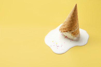 Melted ice cream in wafer cone on yellow background. Space for text