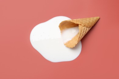 Melted ice cream and wafer cone on pale pink background, top view