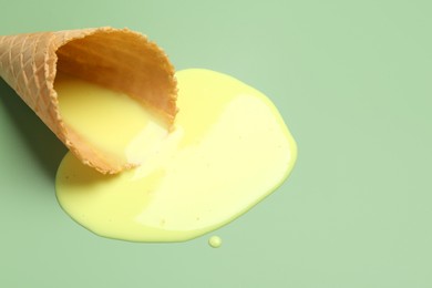 Photo of Melted ice cream and wafer cone on light green background, closeup. Space for text