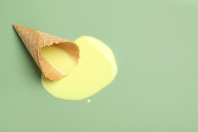 Photo of Melted ice cream and wafer cone on light green background. Space for text