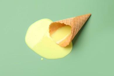 Melted ice cream and wafer cone on light green background