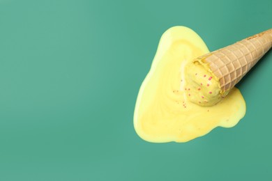 Photo of Melted ice cream in wafer cone on pale green background, top view. Space for text