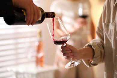 Man pouring red wine into woman`s glass indoors, selective focus