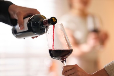 Photo of Man pouring red wine into woman`s glass indoors, selective focus