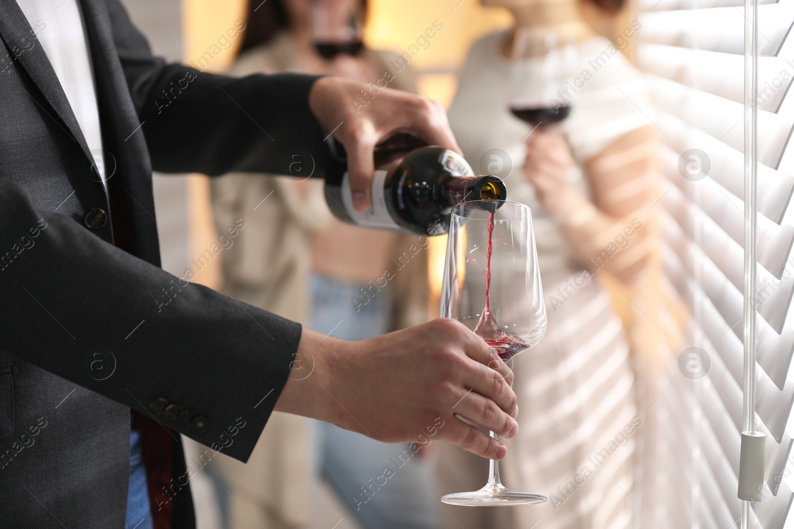 Photo of Man pouring red wine into glass indoors, selective focus