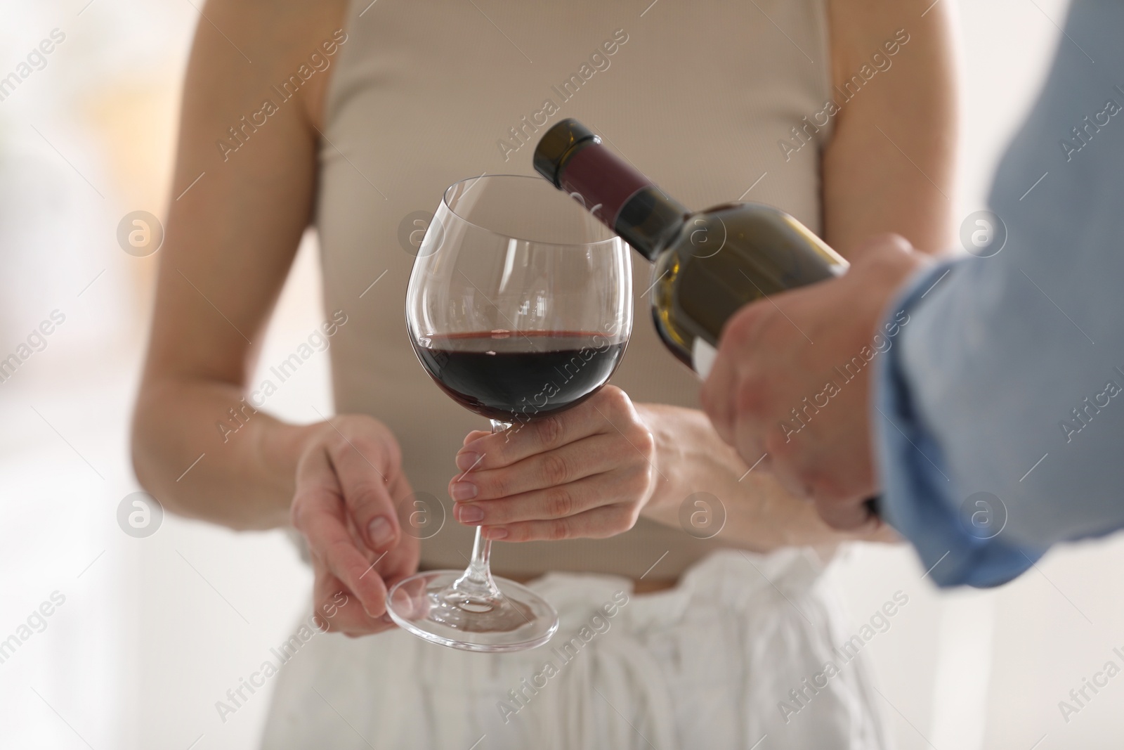 Photo of Man pouring red wine into woman`s glass indoors, closeup