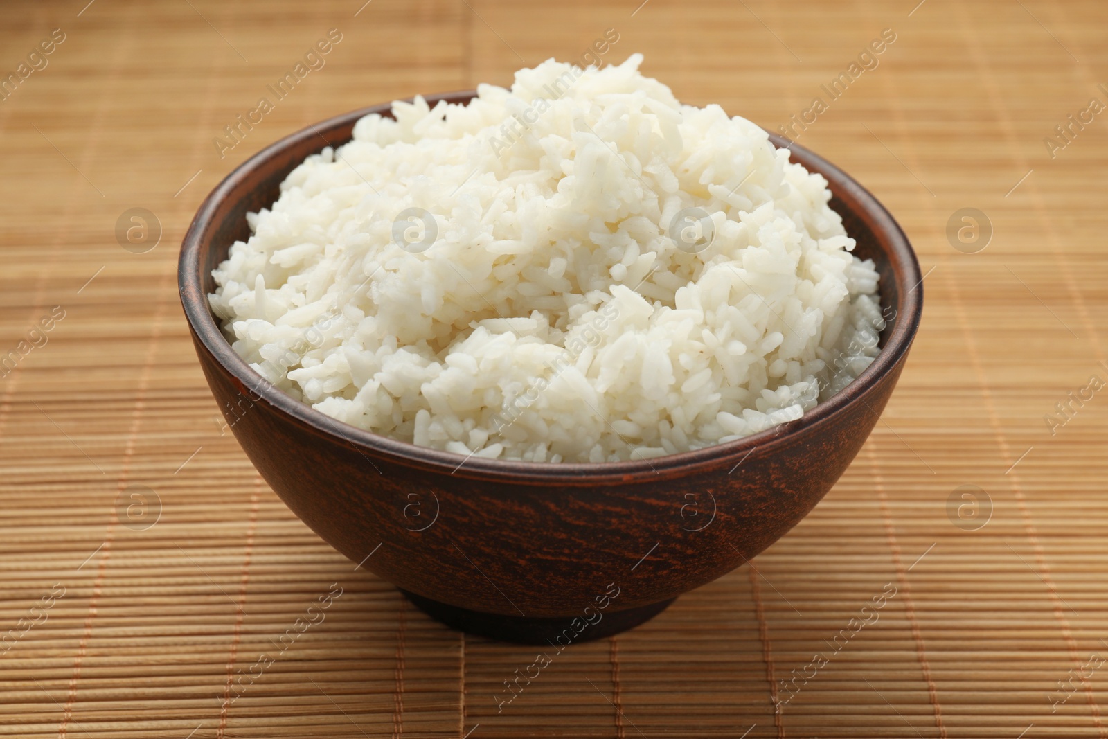 Photo of Tasty cooked rice in bowl on bamboo mat