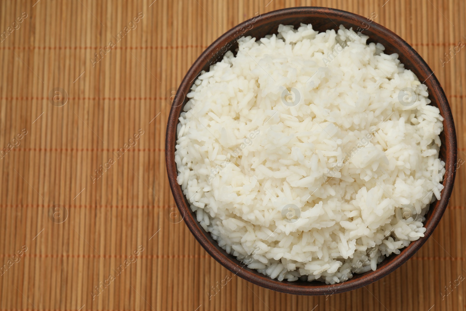 Photo of Tasty cooked rice in bowl on bamboo mat, top view. Space for text