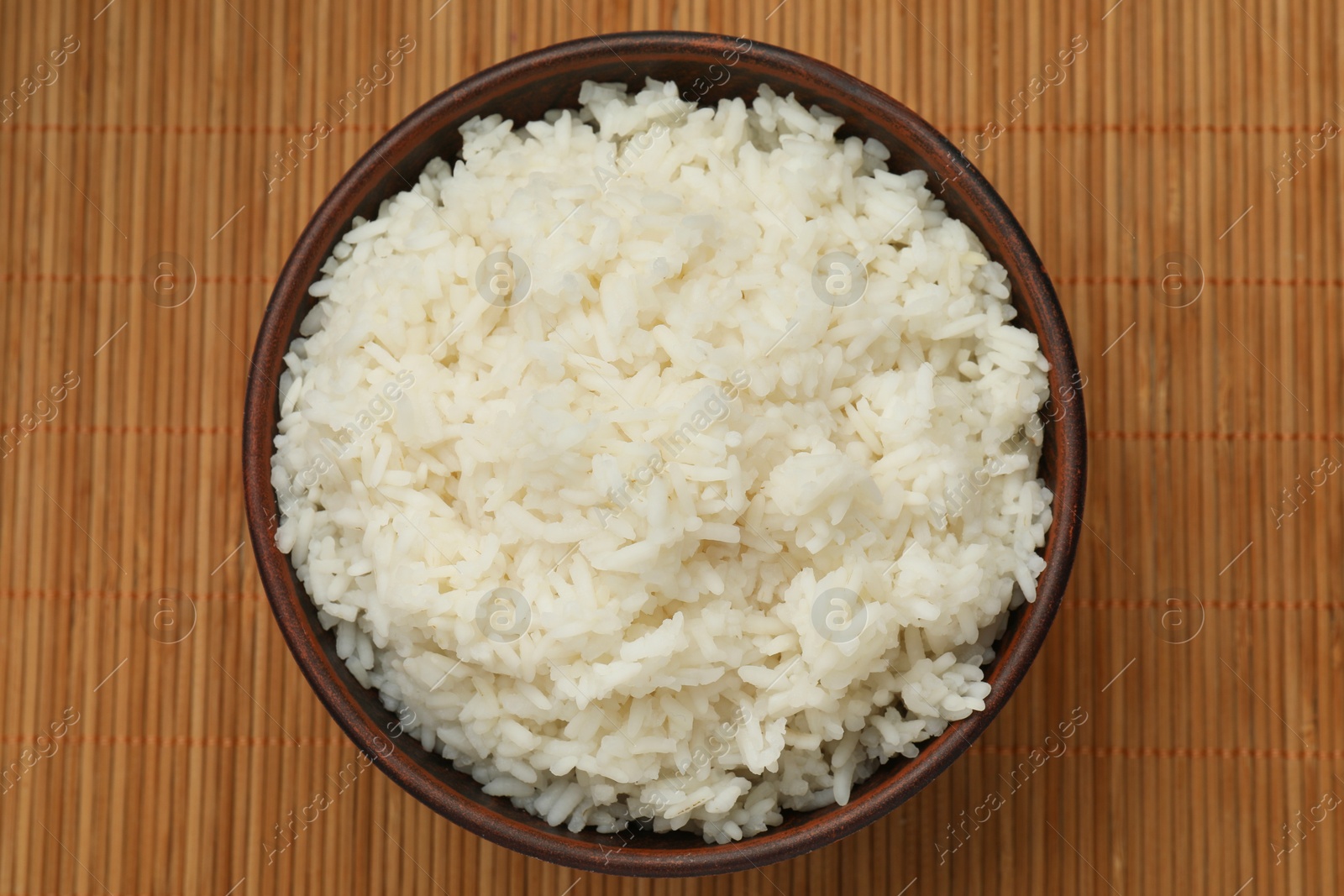 Photo of Tasty cooked rice in bowl on bamboo mat, top view