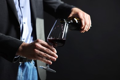 Photo of Man pouring red wine from bottle into glass on black background, closeup. Space for text