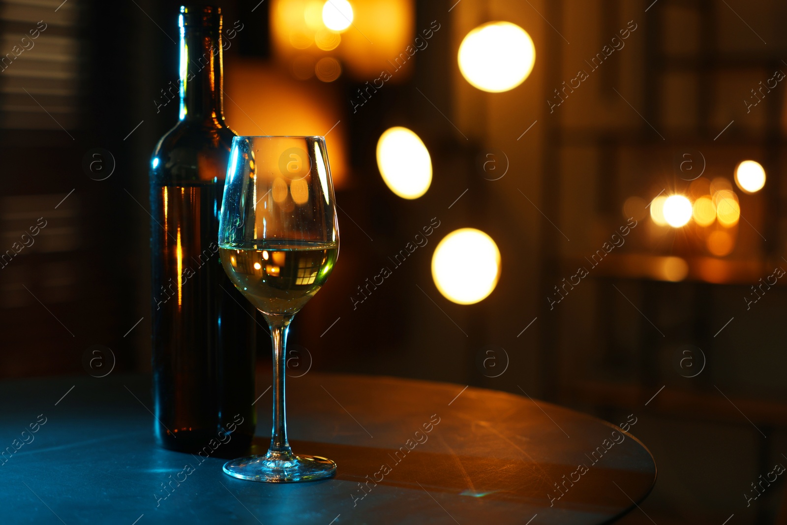 Photo of Tasty wine in glass and bottle on table against blurred lights. Space for text