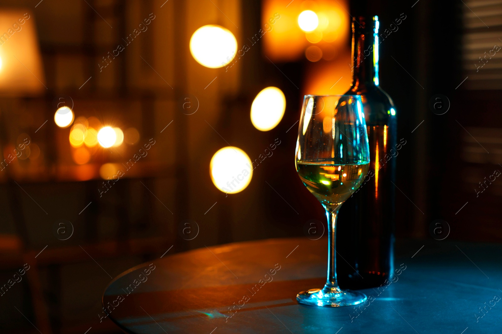 Photo of Tasty wine in glass and bottle on table against blurred lights. Space for text