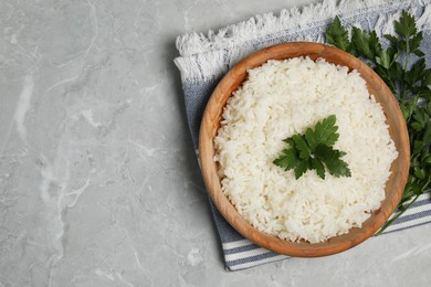 Tasty cooked rice in bowl with parsley on grey marble table, flat lay. Space for text