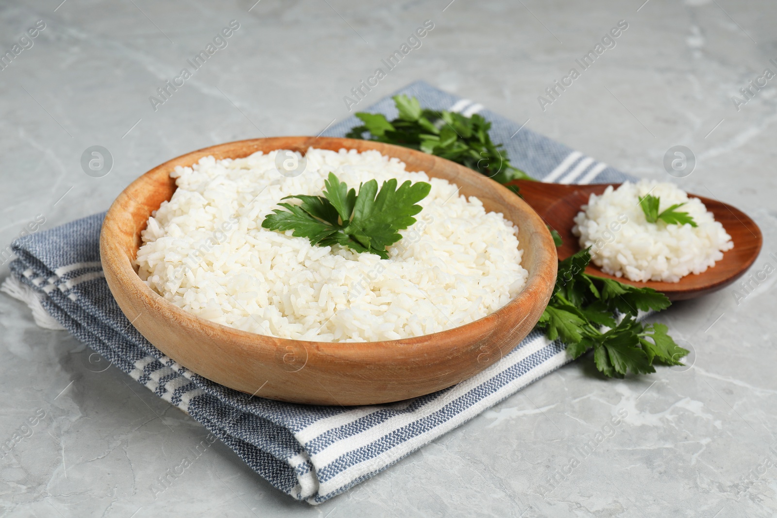 Photo of Tasty cooked rice in bowl with parsley and spoon on grey marble table