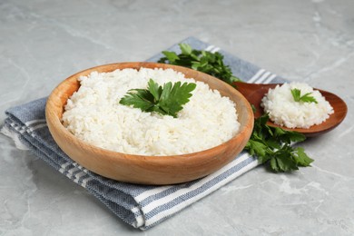 Tasty cooked rice in bowl with parsley and spoon on grey marble table