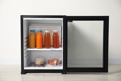 Mini refrigerator with different drinks and snacks near white wall