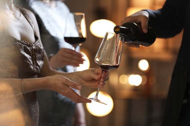 Man pouring wine into woman`s glass indoors, selective focus