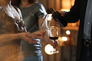 Man pouring wine into woman`s glass indoors, selective focus