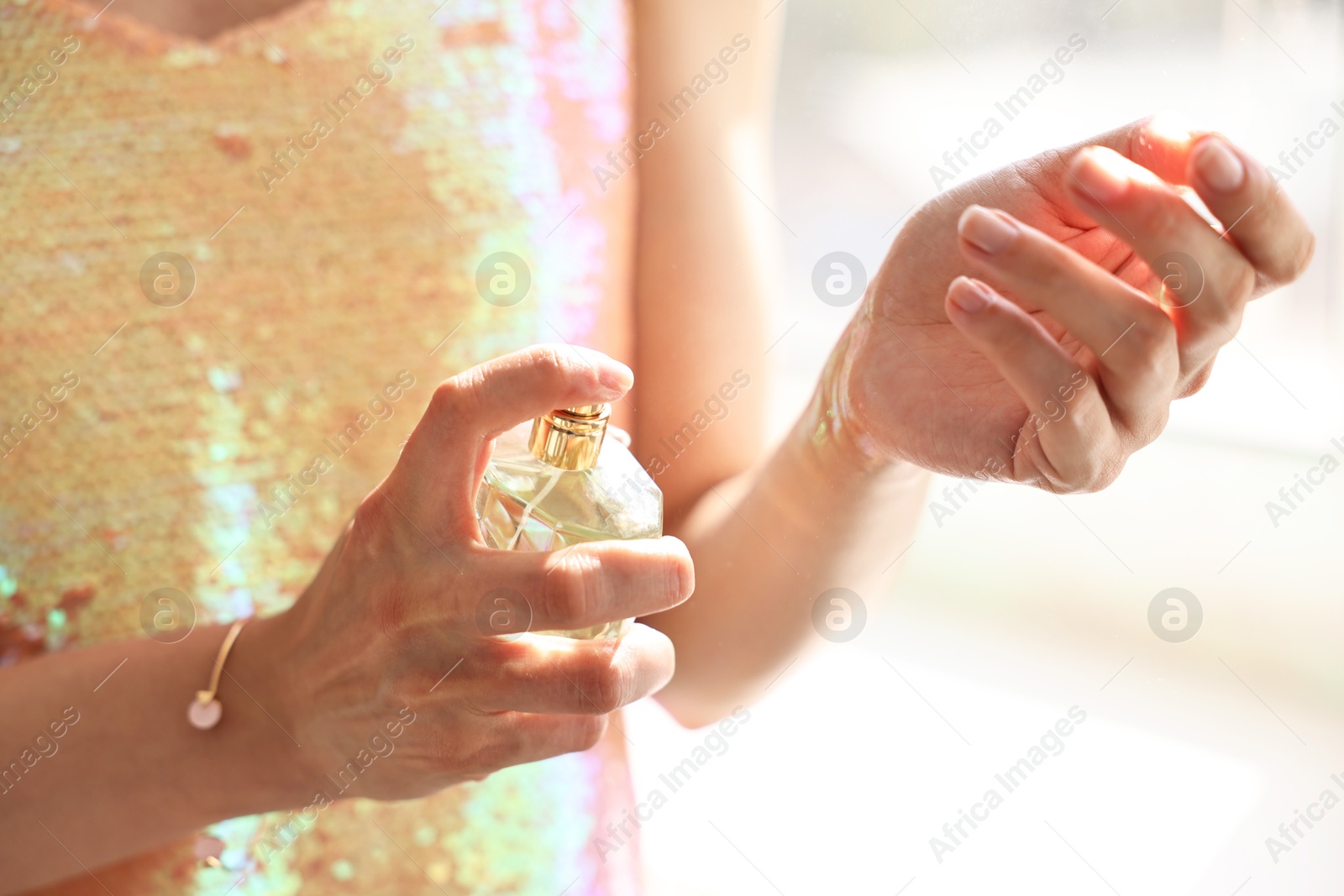 Photo of Woman spraying perfume onto wrist indoors, closeup