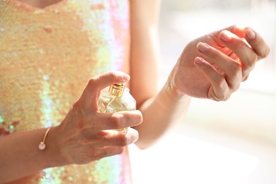 Photo of Woman spraying perfume onto wrist indoors, closeup