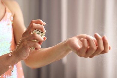 Photo of Woman spraying perfume onto wrist indoors, closeup