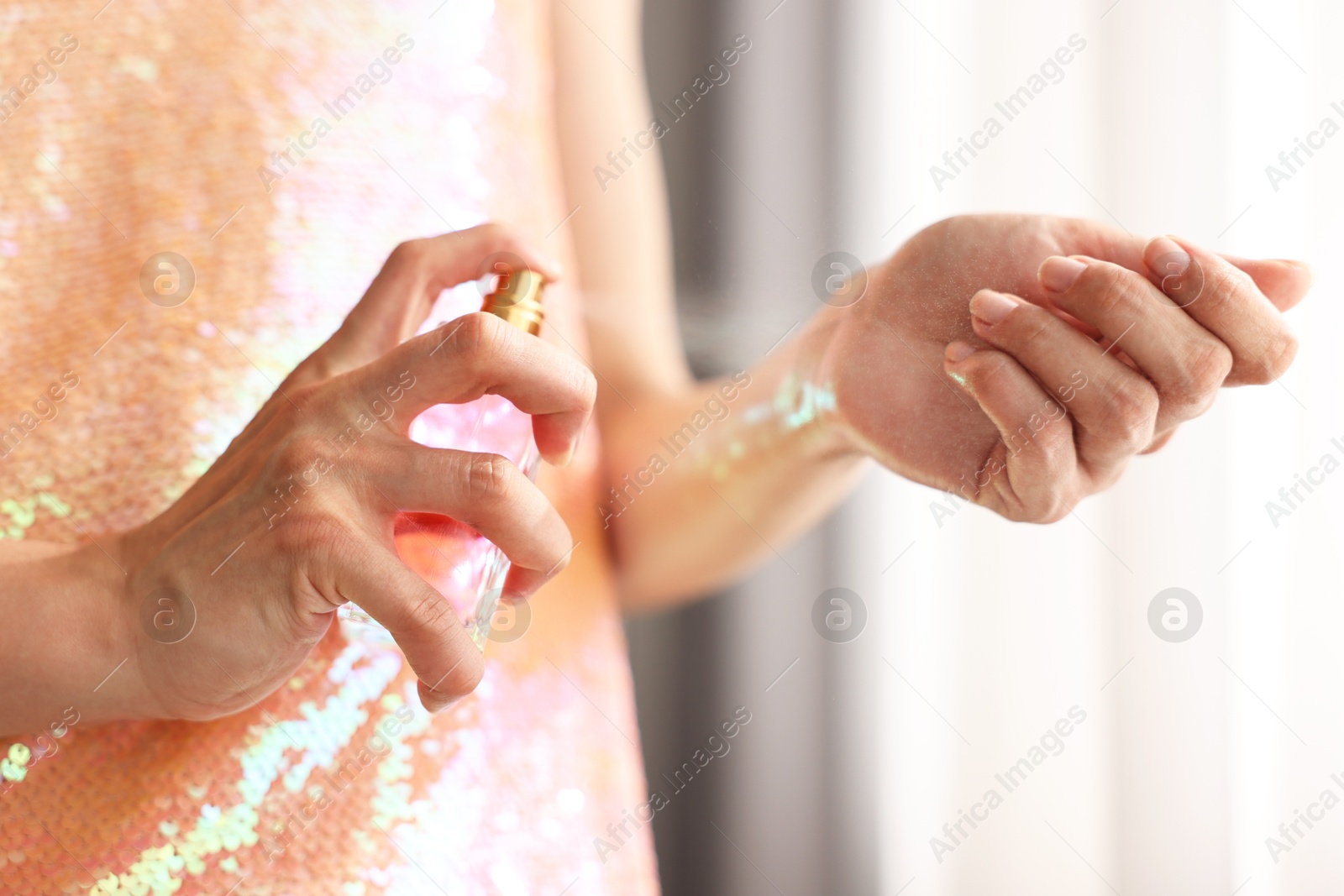 Photo of Woman spraying perfume onto wrist indoors, closeup