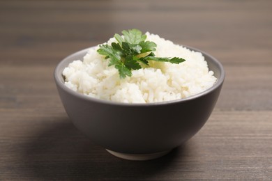 Photo of Bowl of delicious boiled rice with parsley on wooden table