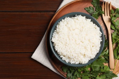 Photo of Delicious boiled rice served with parsley on wooden table, top view. Space for text