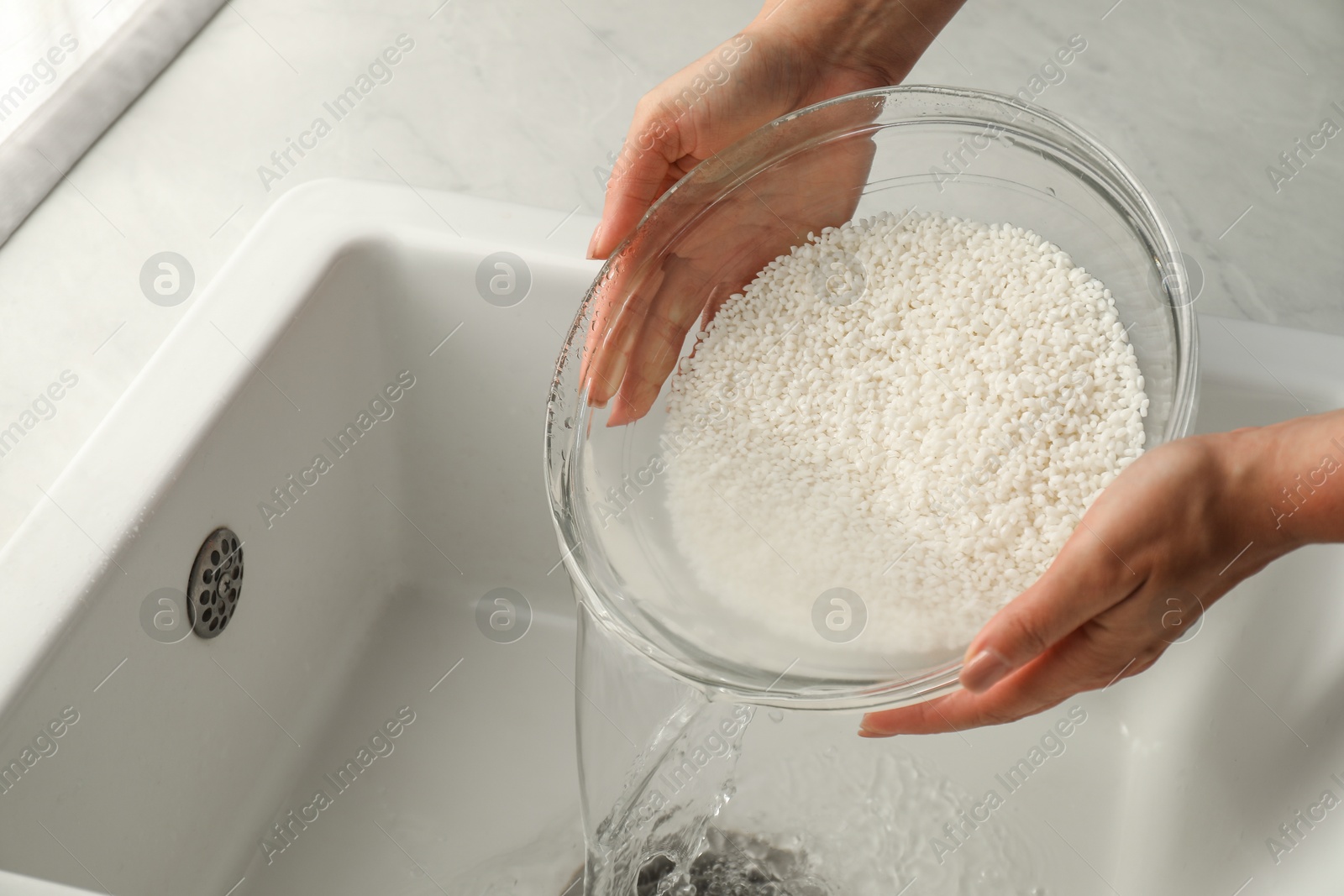 Photo of Woman rinsing rice in bowl above sink, closeup