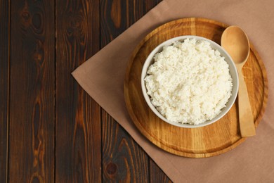 Photo of Delicious boiled rice in bowl and spoon on wooden table, top view. Space for text