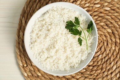 Photo of Delicious boiled rice in bowl and parsley on wooden table, top view