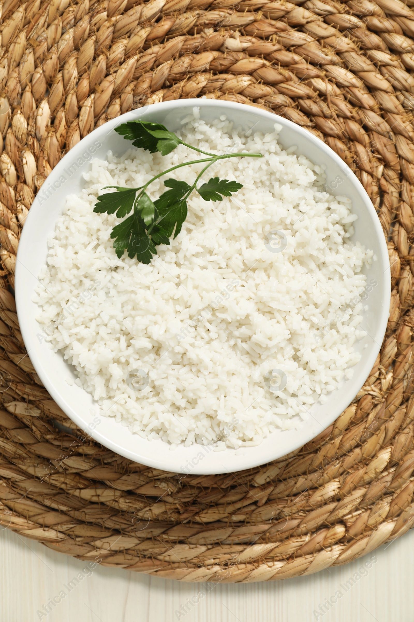 Photo of Delicious boiled rice in bowl and parsley on wooden table, top view