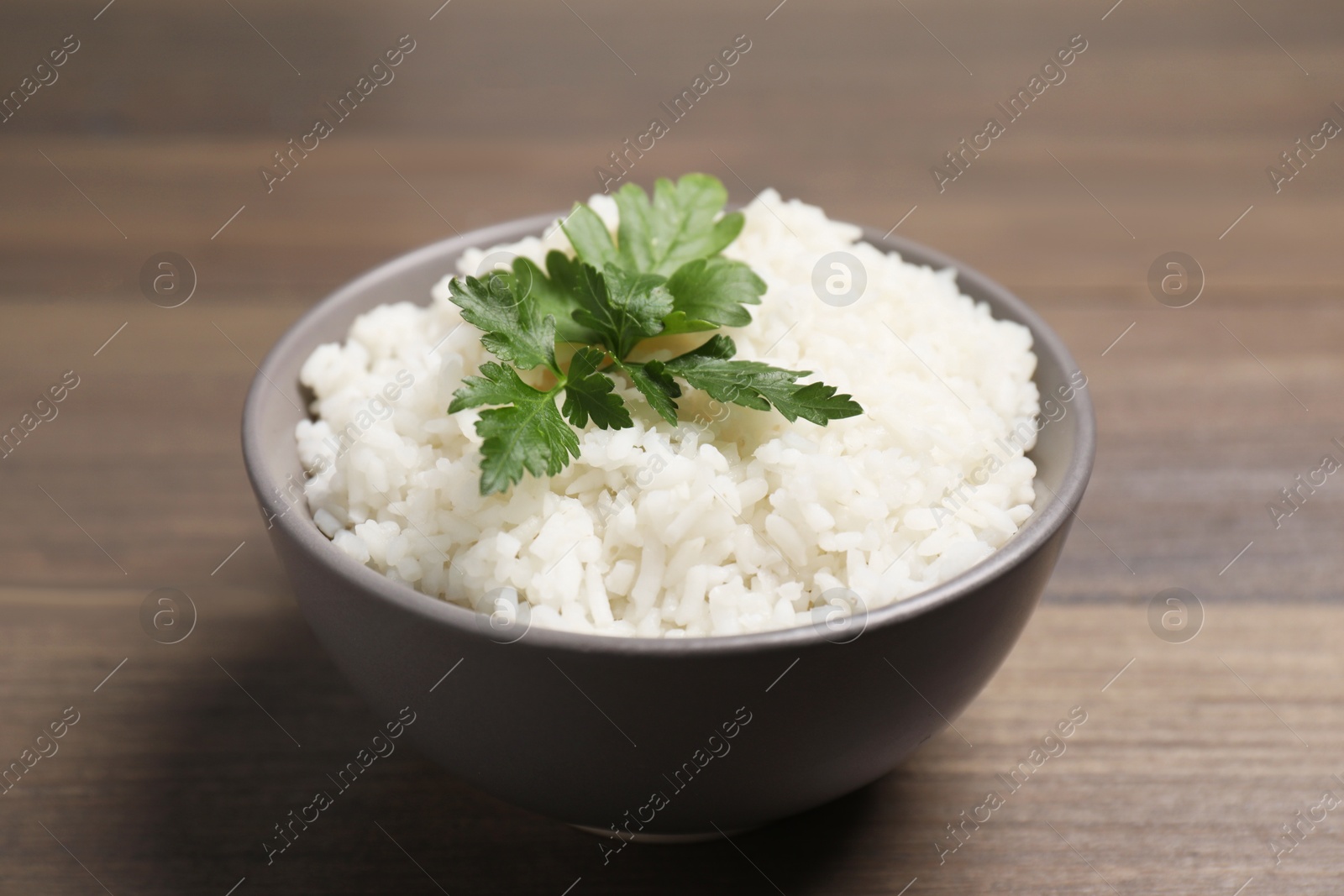 Photo of Bowl of delicious boiled rice with parsley on wooden table, closeup