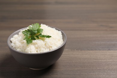 Photo of Bowl of delicious boiled rice with parsley on wooden table. Space for text