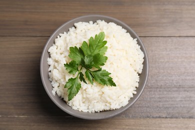 Photo of Bowl of delicious boiled rice with parsley on wooden table, top view