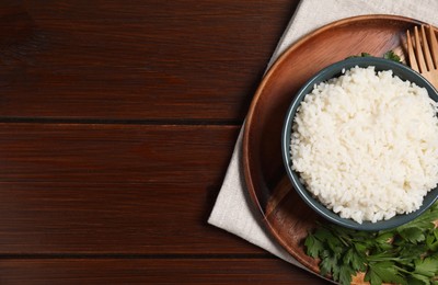 Photo of Delicious boiled rice served with parsley on wooden table, top view. Space for text