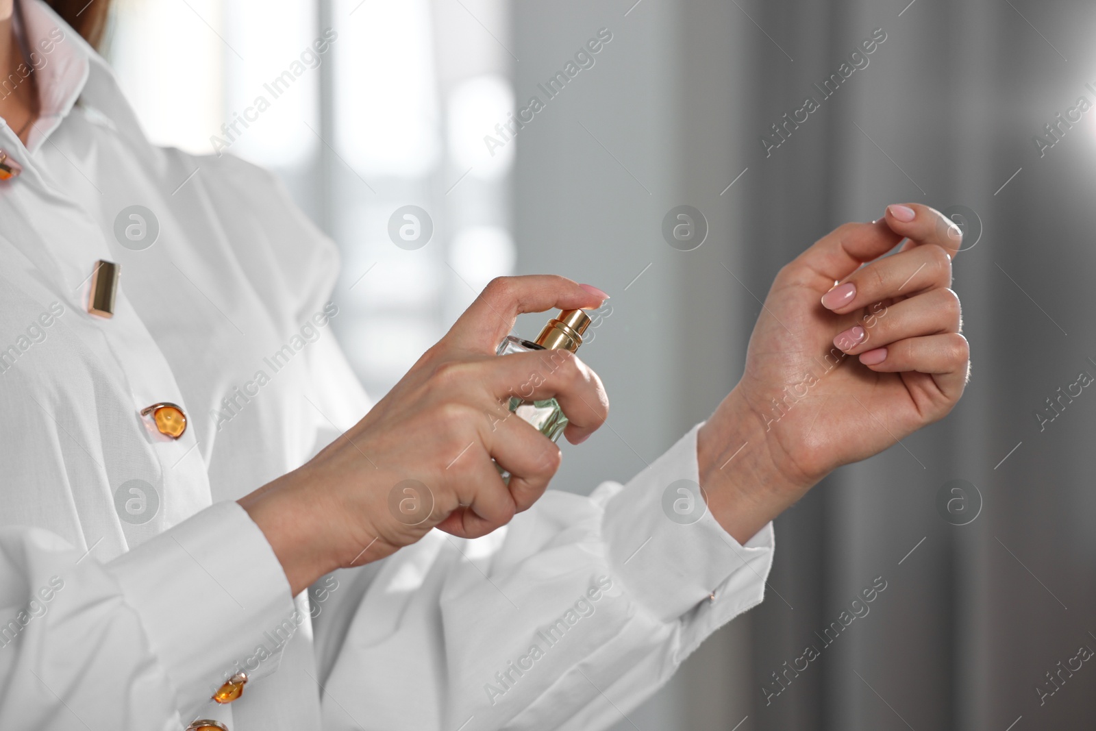 Photo of Woman spraying perfume onto wrist indoors, closeup