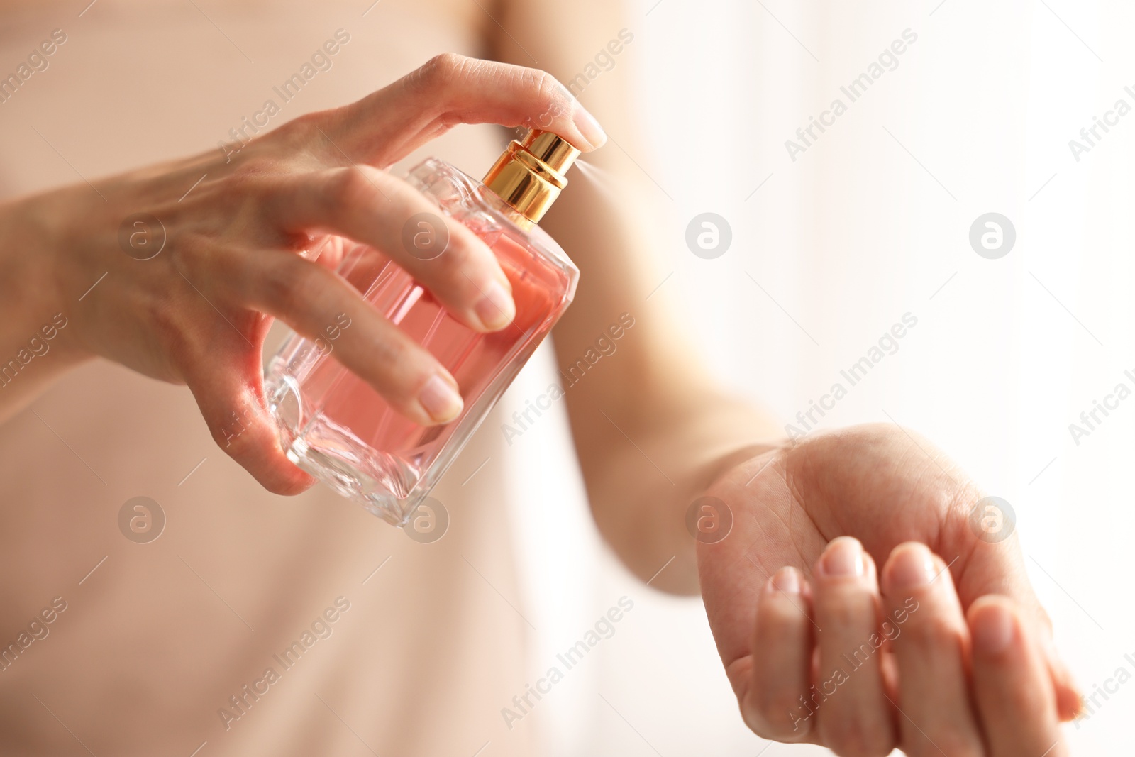 Photo of Woman spraying perfume onto wrist indoors, closeup