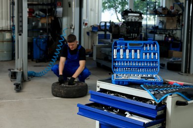 Photo of Auto mechanic with tire, focus on different tools at automobile repair shop