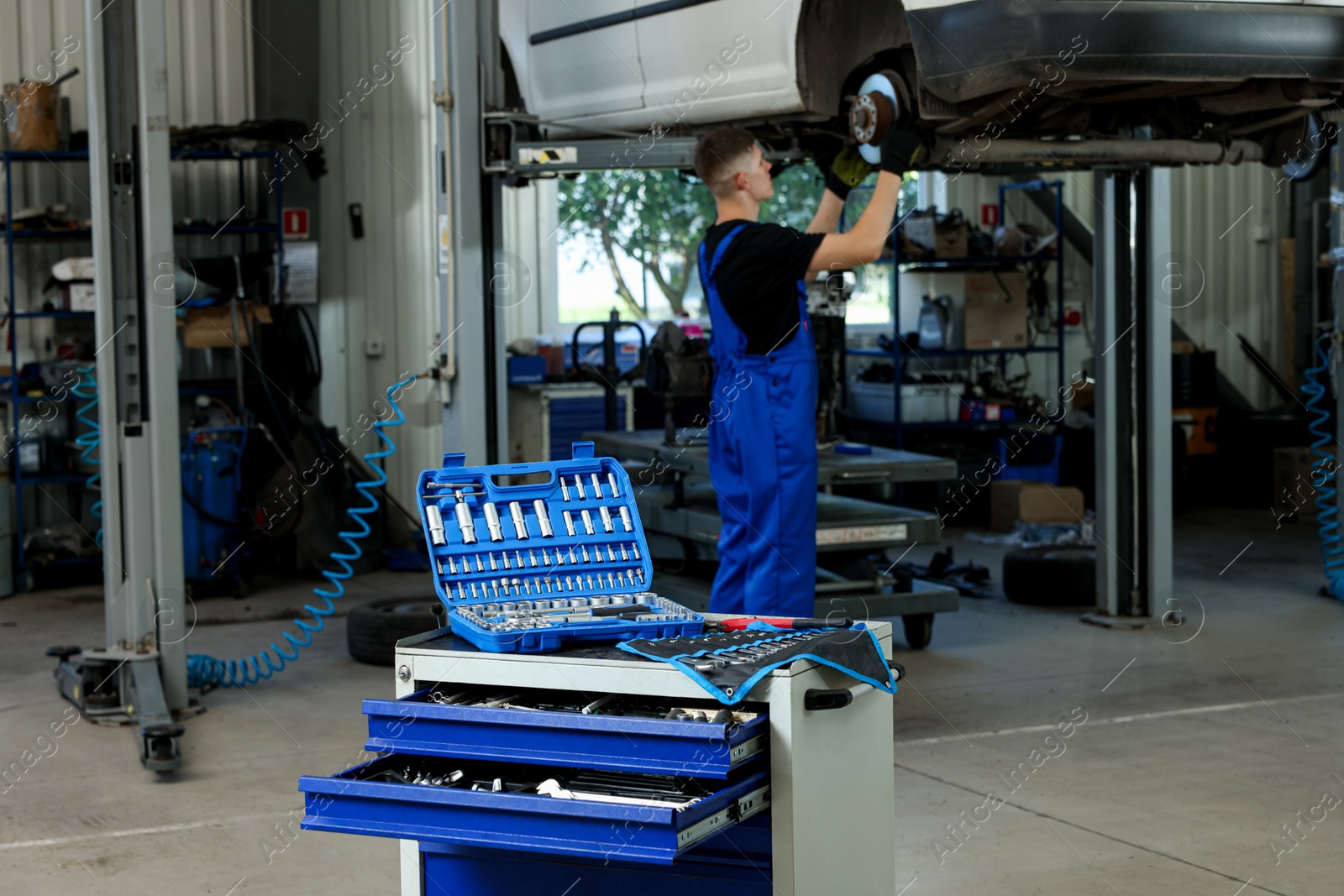 Photo of Auto mechanic fixing lifted car at automobile repair shop, focus on different tools