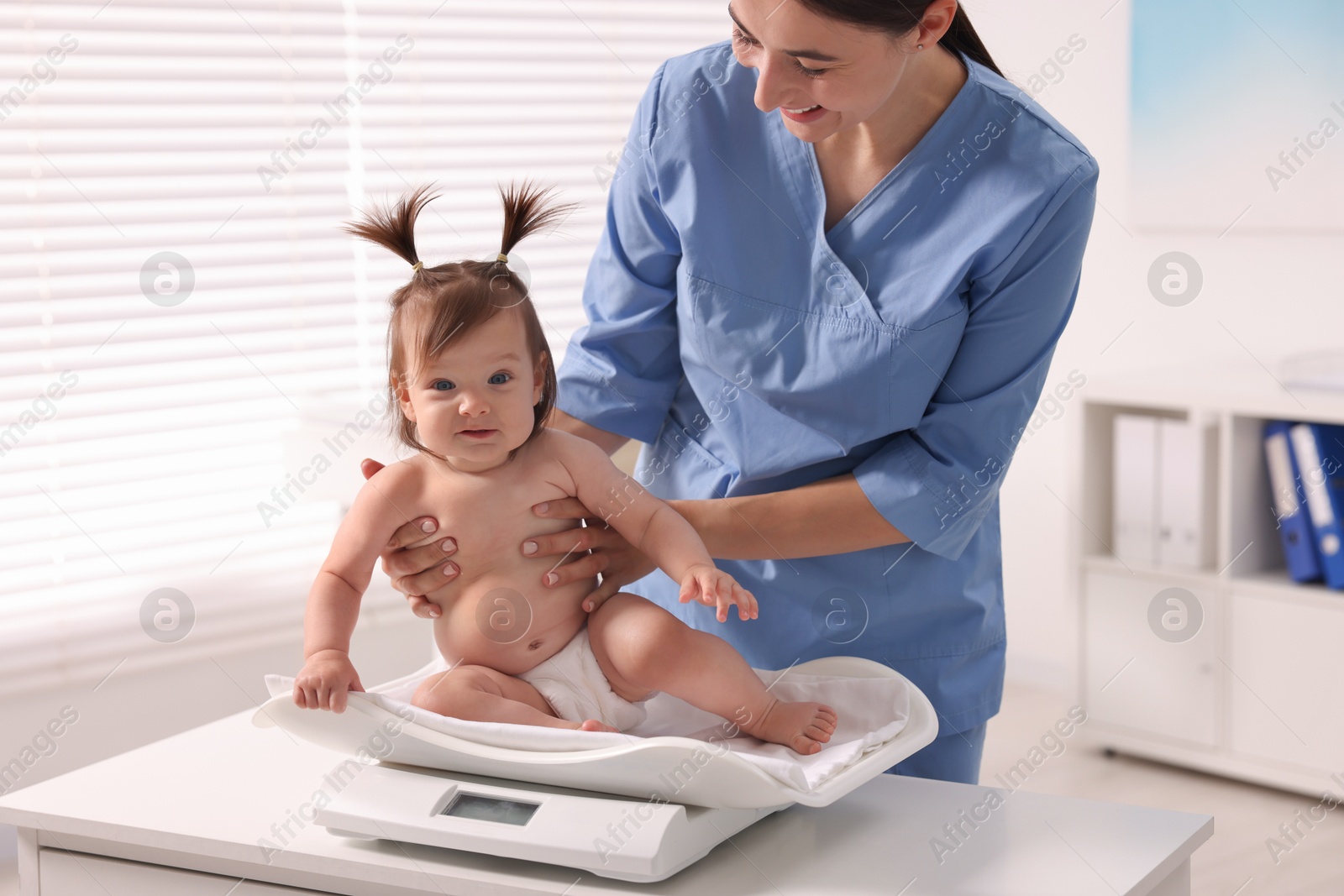 Photo of Pediatrician weighting cute little girl in clinic. Checking baby's health