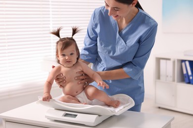 Photo of Pediatrician weighting cute little girl in clinic. Checking baby's health